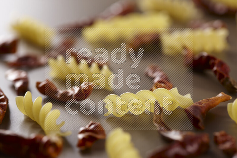 Raw pasta with different ingredients such as cherry tomatoes, garlic, onions, red chilis, black pepper, white pepper, bay laurel leaves, rosemary and cardamom on beige background