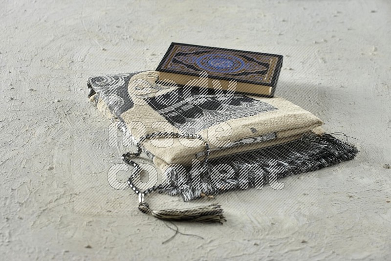 A prayer rug with different elements such as quran and prayer beads on white textured background