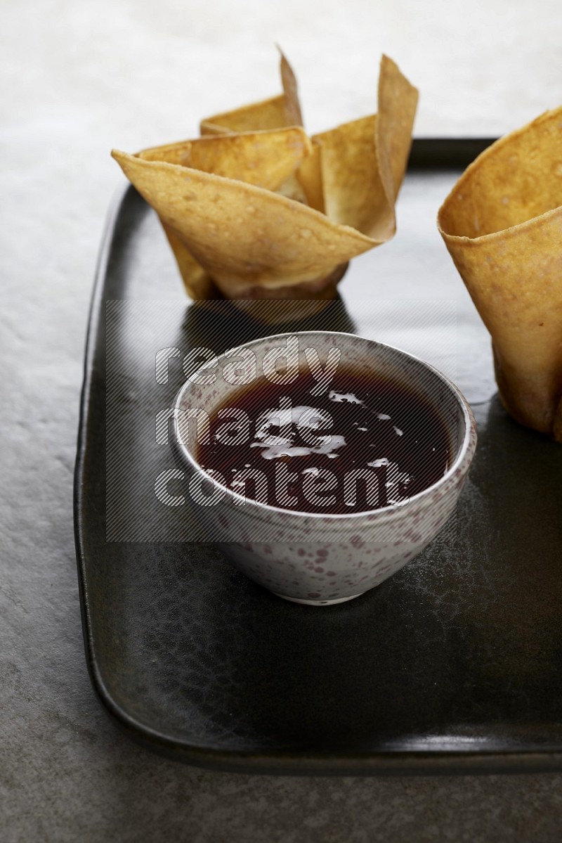 wonton cups with soy sauce ramkin on rectangle dark grey ceramic plate on grey textured counter top