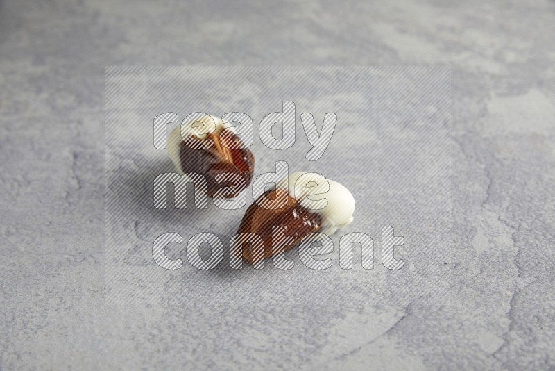 two almonds stuffed dates covered with white chololate on a light grey background