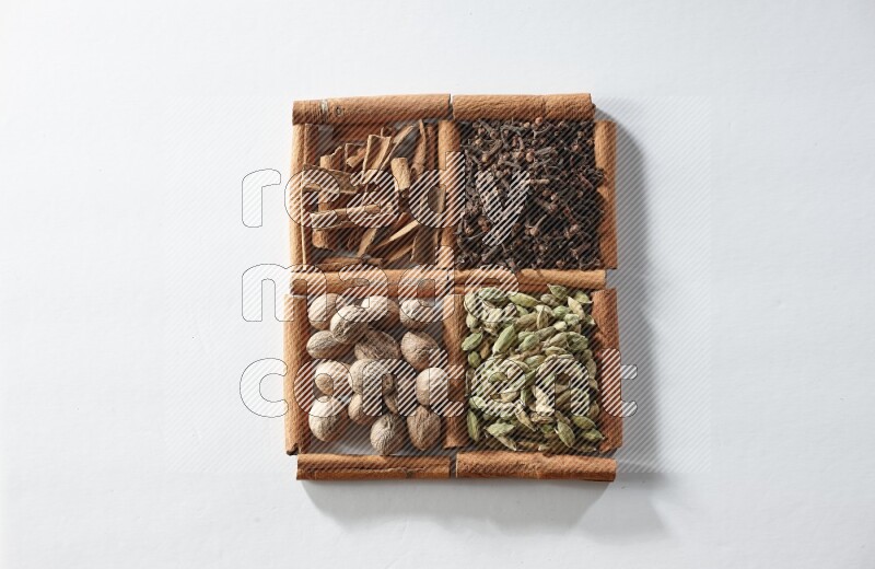 4 مربعات من أعواد القرفة ممتلئة بالهيل والقرفة والقرنفل وجوزة الطيب على أرضية بيضاء