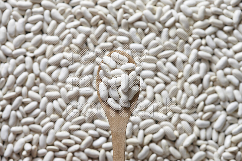 A wooden spoon full of white beans on white beans background