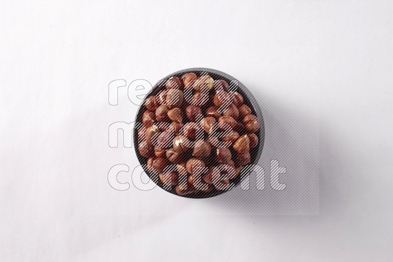 Hazelnuts in a black pottery bowl on white background