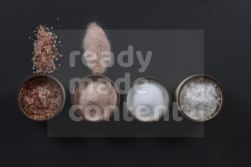 4 pottery bowls filled with himalayan salt and white salt on black background