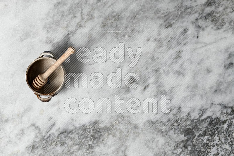 Multicolored Pottery Bowl with wooden honey handle in it, on grey marble flooring, Top View