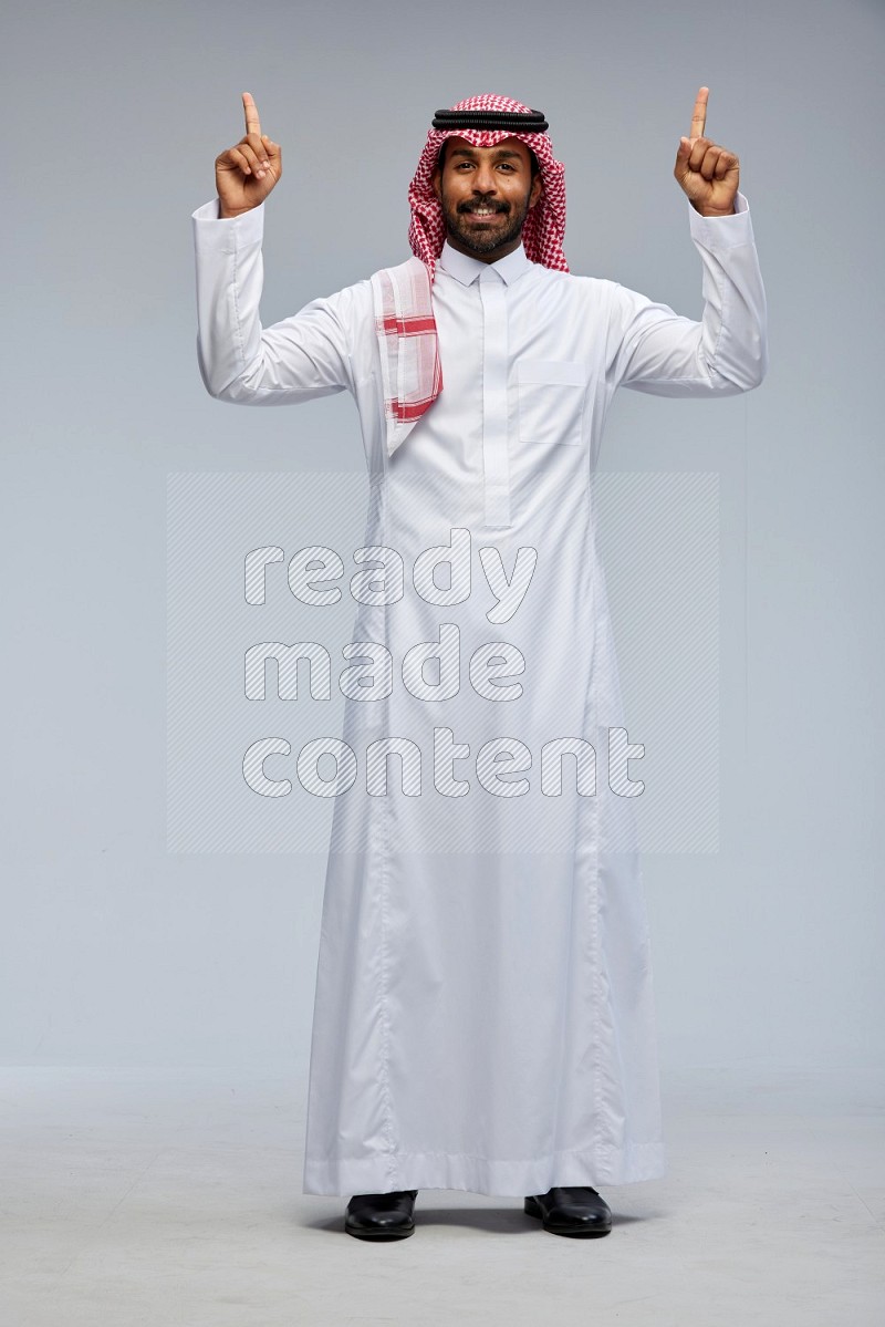 Saudi man Wearing Thob and shomag standing interacting with the camera on Gray background