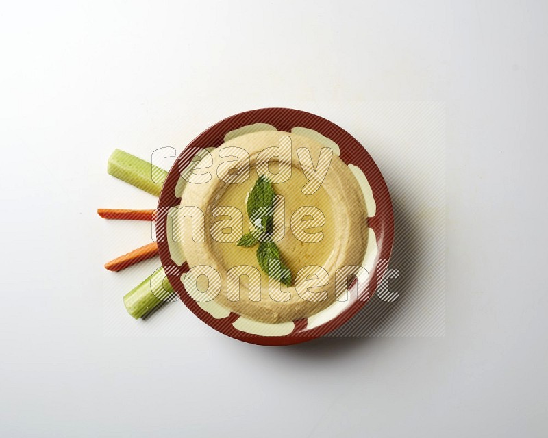 Hummus in a traditional plate garnished with mint on a white background