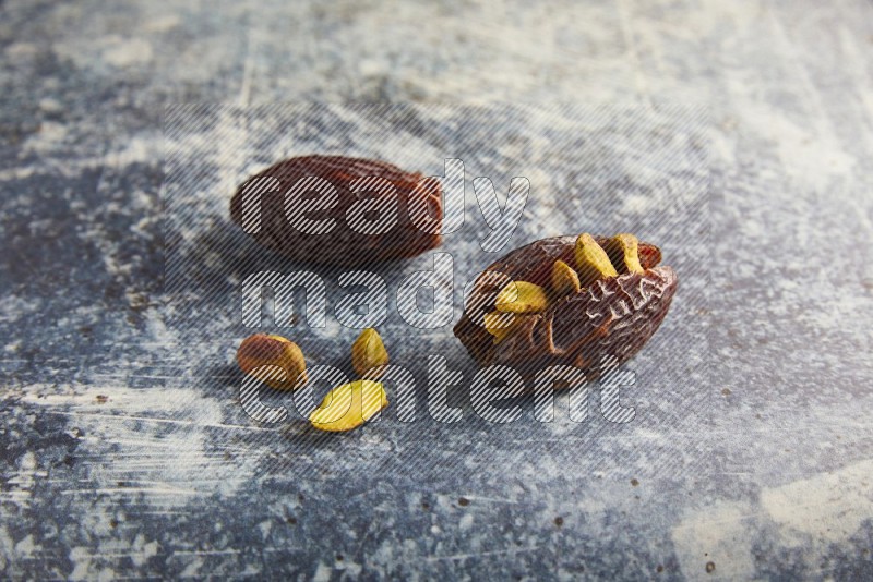 two pistachios stuffed madjoul dates on a rustic blue background