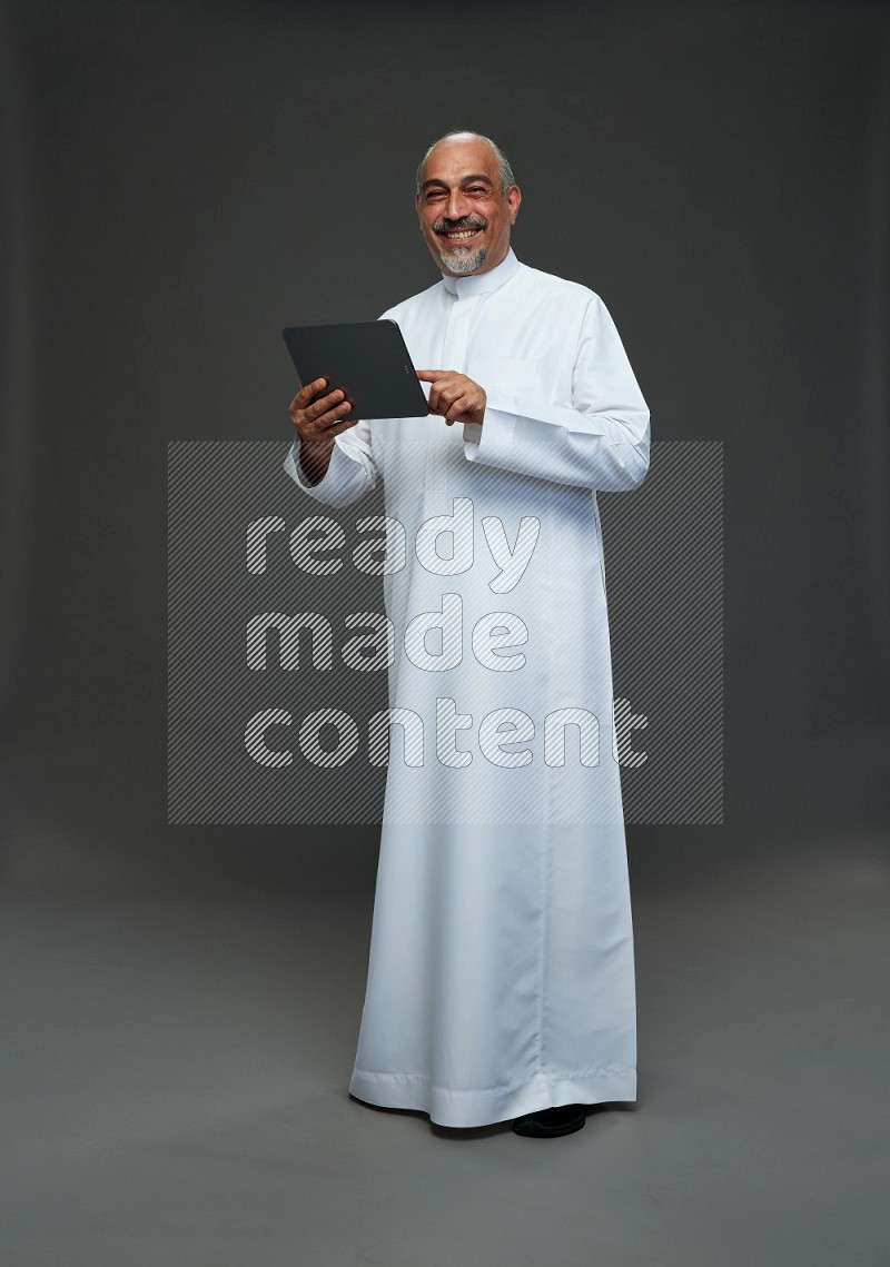 Saudi man without shomag Standing working on tablet on gray background