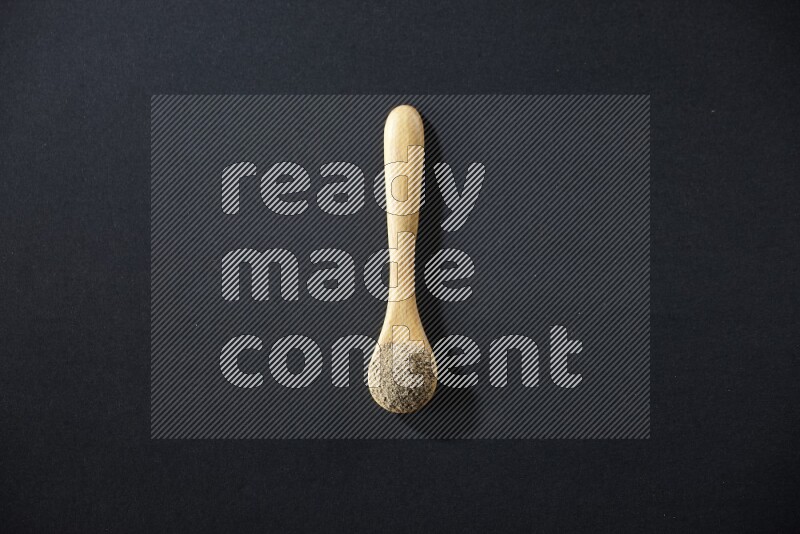 ملعقة خشبية ممتلئة ببودرة الهيل على خلفية سوداء