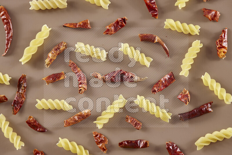 Raw pasta with different ingredients such as cherry tomatoes, garlic, onions, red chilis, black pepper, white pepper, bay laurel leaves, rosemary and cardamom on beige background