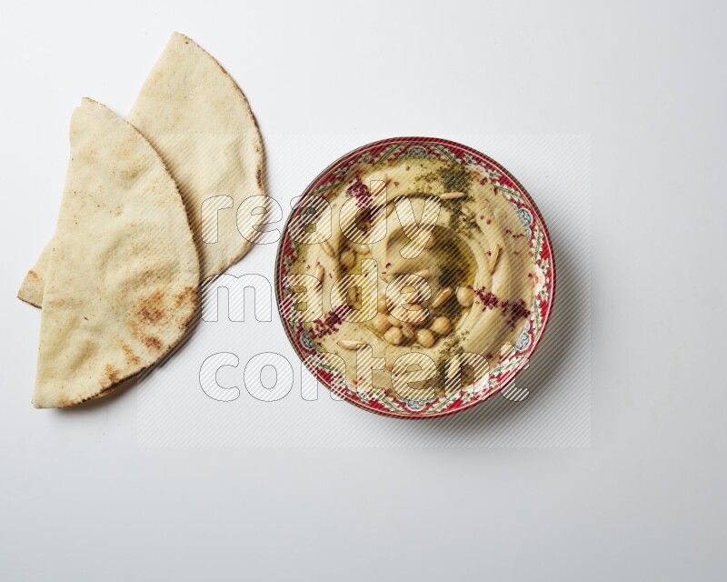 Hummus in a red plate with patterns garnished with zaatar & sumak on a white background