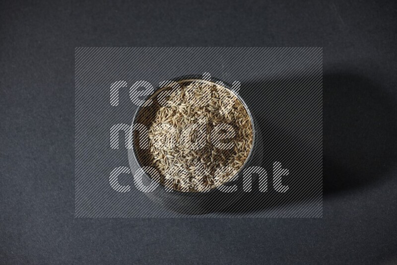 وعاء فخاري أسود ممتلئ بحبوب الكمون على خلفية سوداء