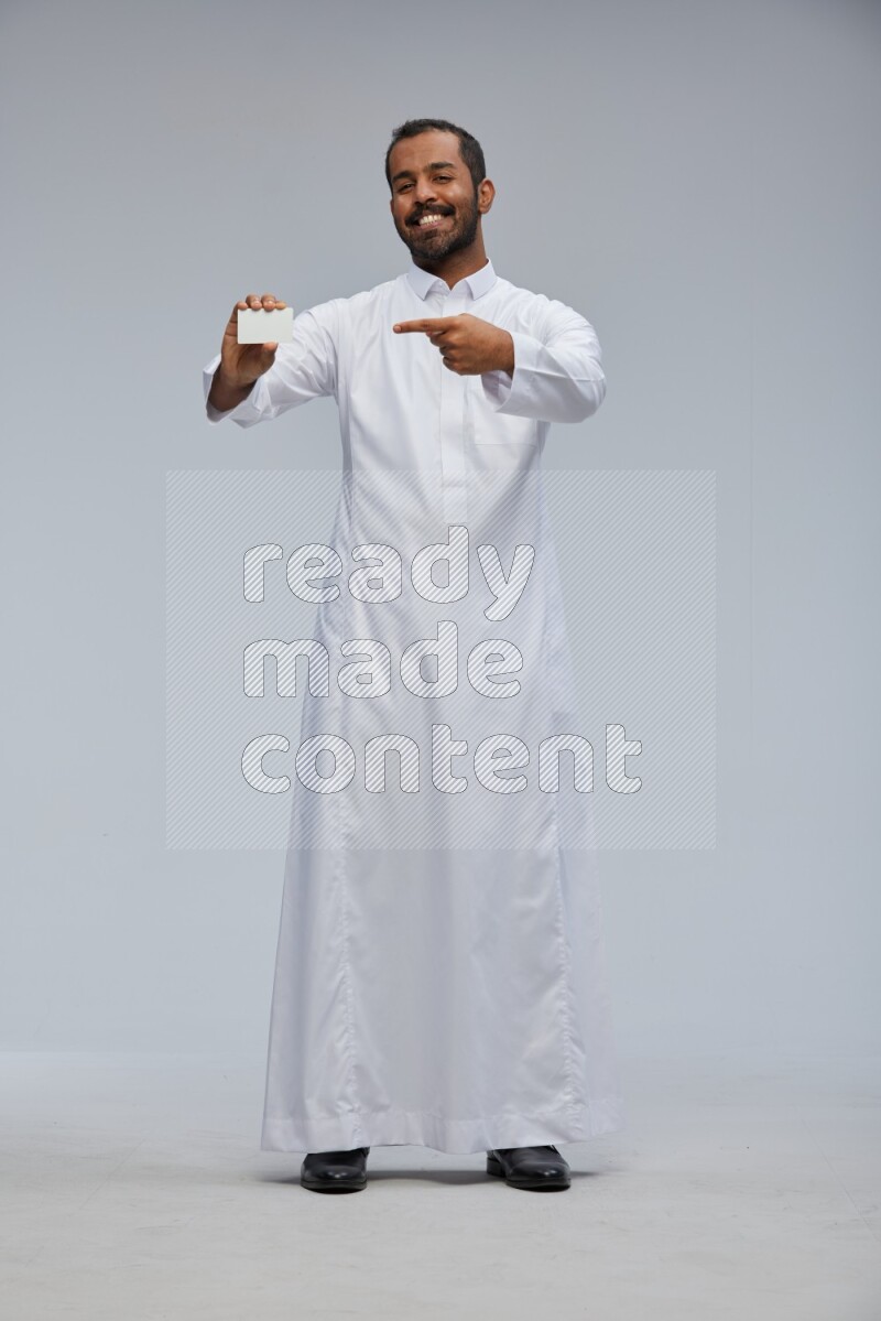 Saudi man wearing Thob standing holding ATM card on Gray background