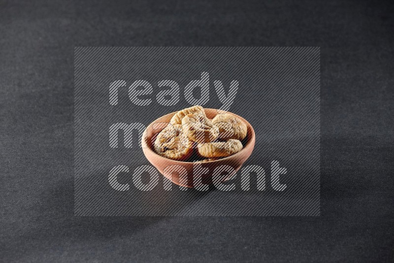 A wooden bowl full of dried figs on a black background in different angles
