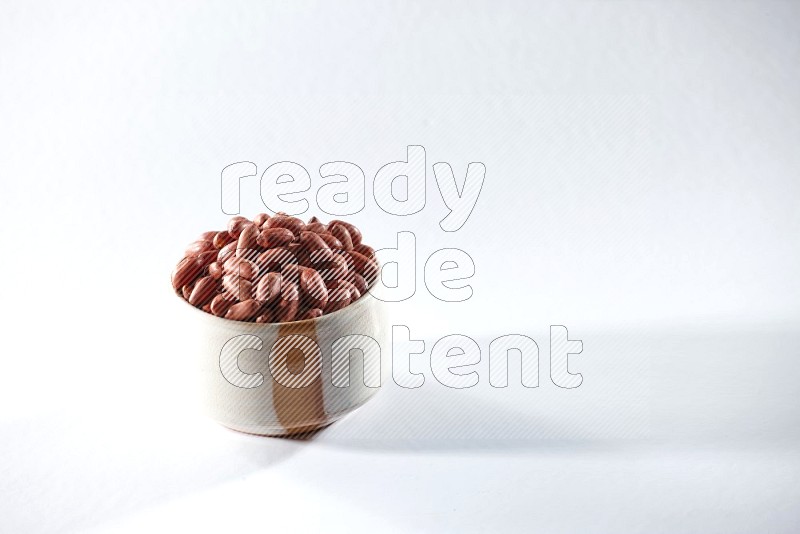 A beige ceramic bowl full of red skin peanuts on a white background in different angles
