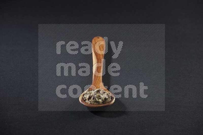 A wooden ladle full of cardamom on black flooring