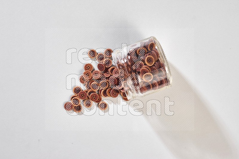 A glass jar full of colored buttons on grey background