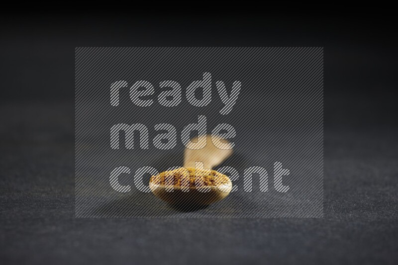 A wooden spoon full of turmeric powder on black flooring