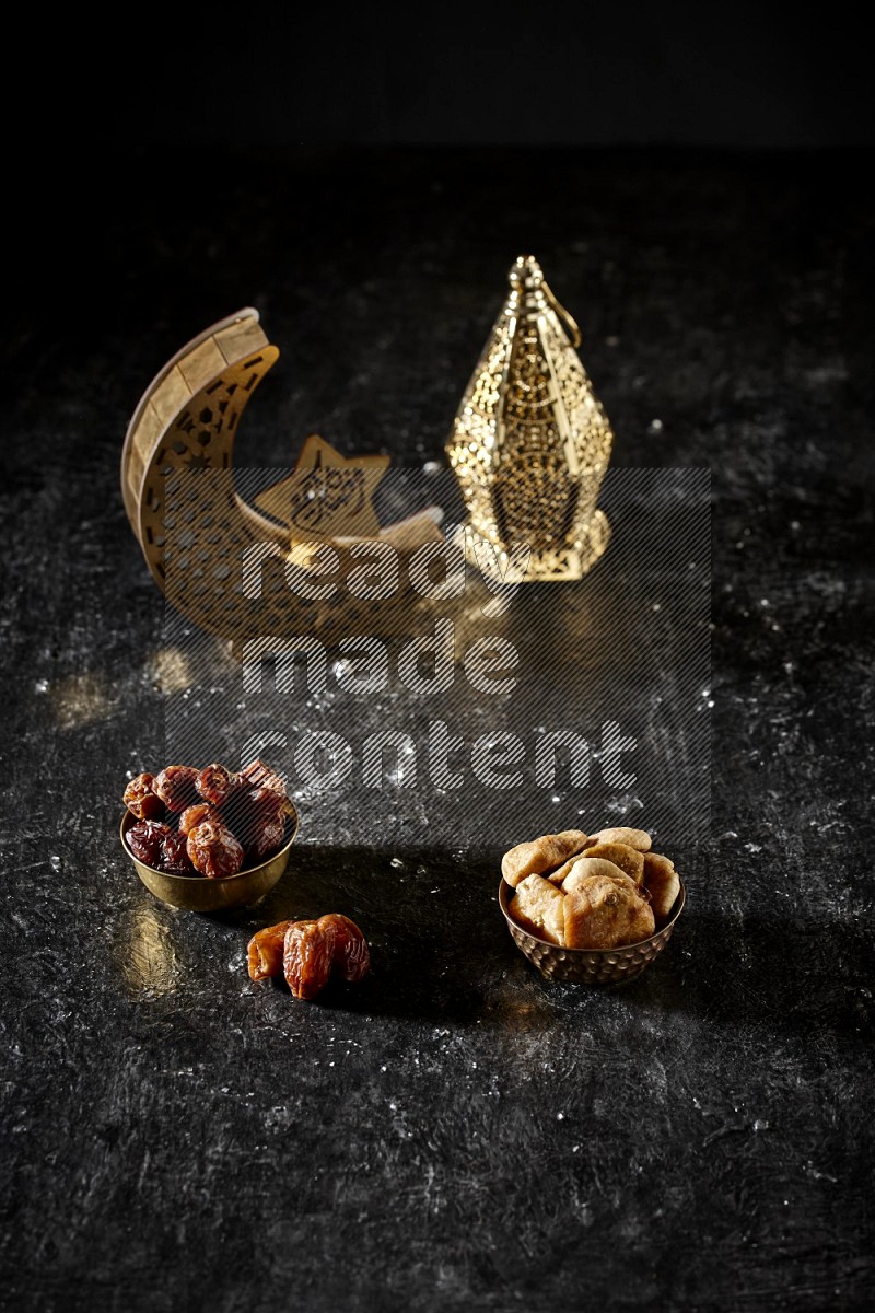 Dates in a metal bowl with dried figs beside golden lanterns in a dark setup