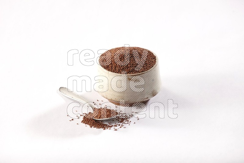 A beige pottery bowl and a metal spoon full of garden cress seeds on a white flooring