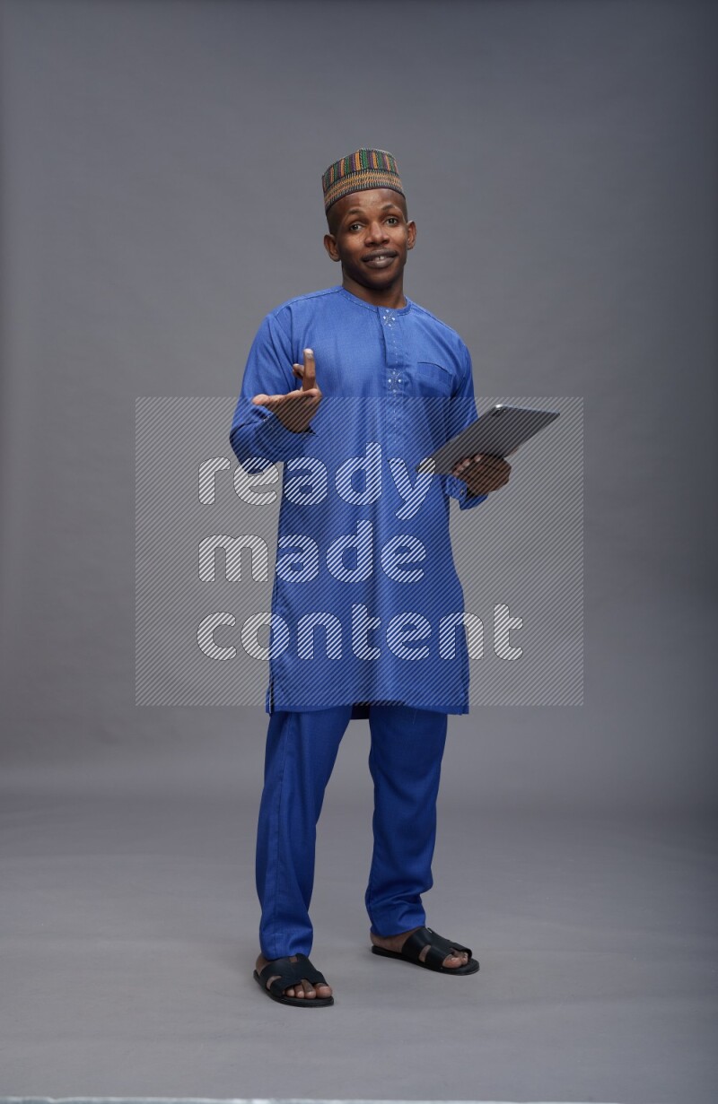 Man wearing Nigerian outfit standing working on tablet on gray background