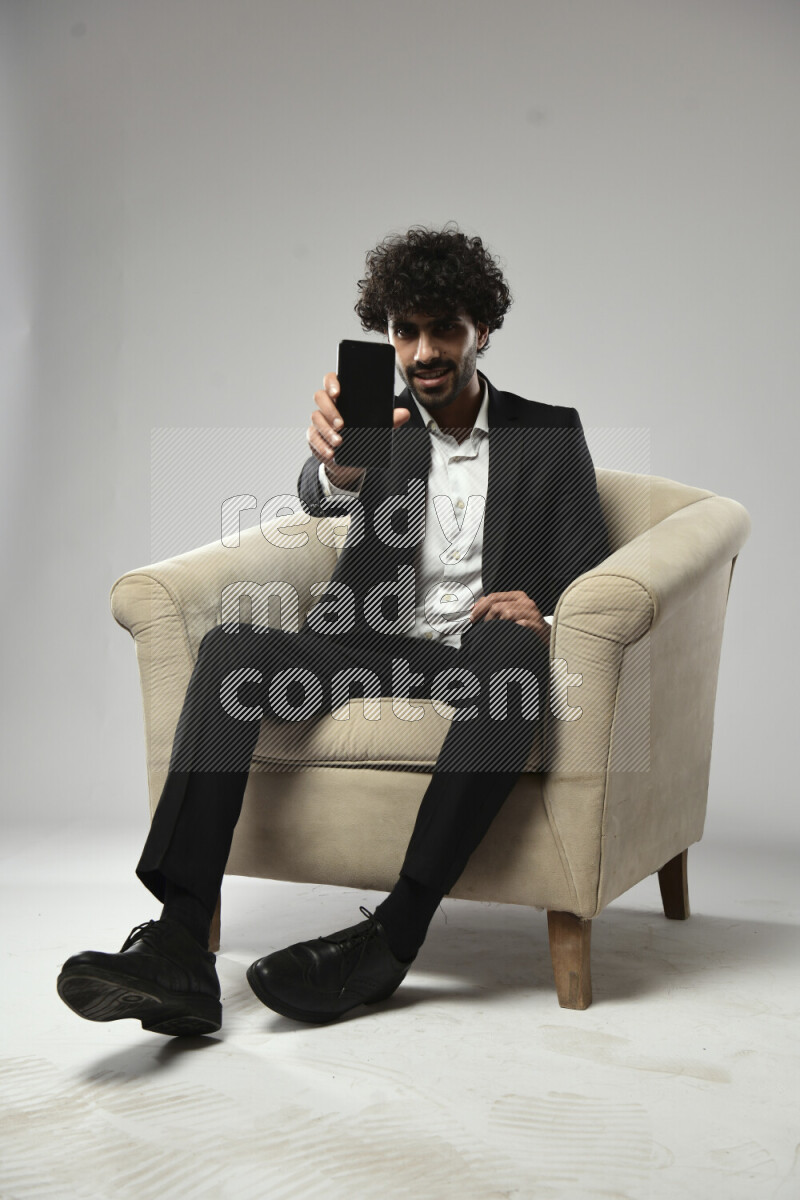 A man wearing formal sitting on a chair showing a phone screen on white background