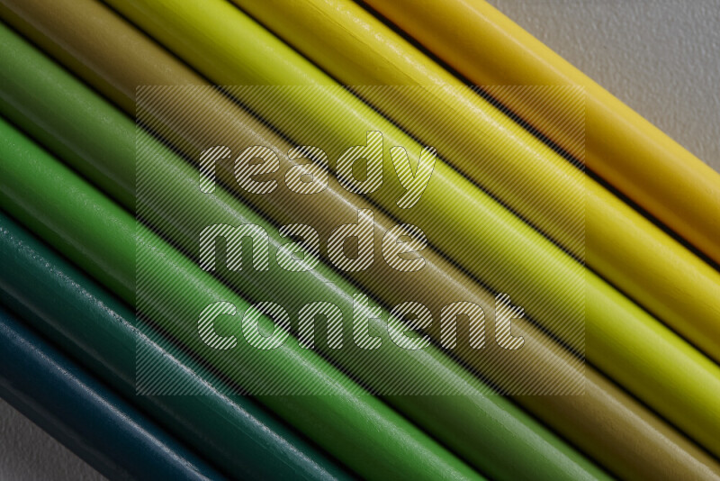 مجموعة من أقلام الرصاص الملونة مرتبة لتعرض تدرجا من اللون الأصفر والأخضر علي خلفية رمادية