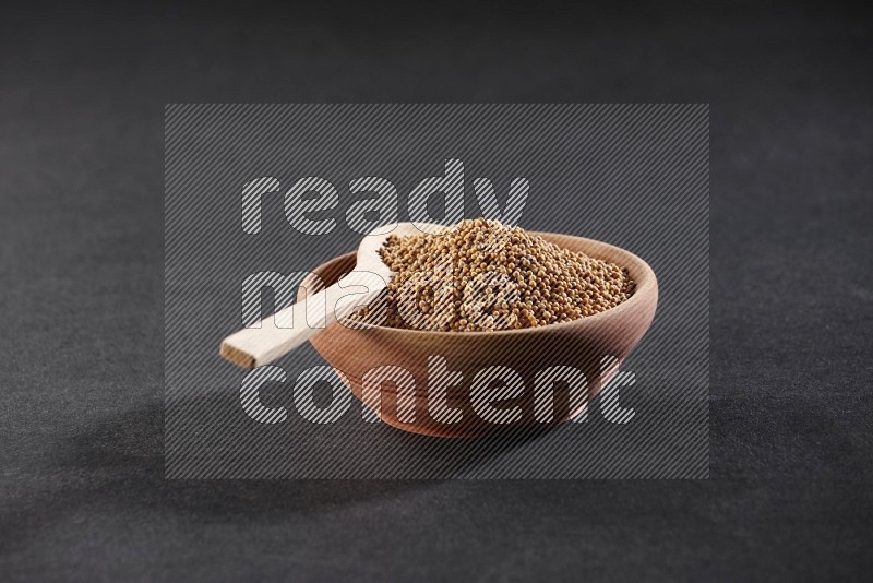 A wooden bowl and spoon full of mustard seeds on a black flooring in different angles
