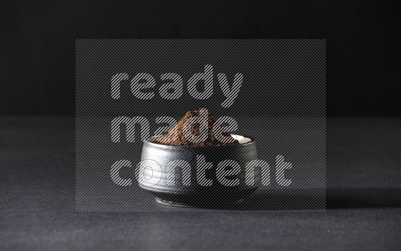 A black pottery bowl full of cloves powder on a black flooring