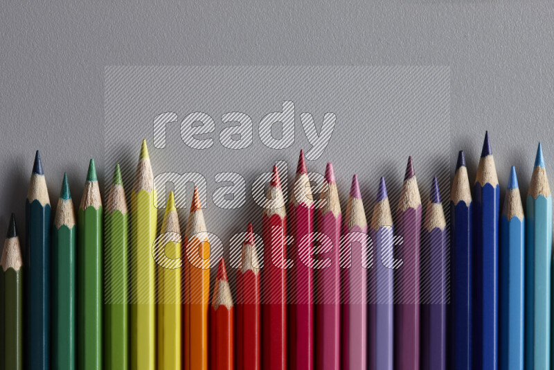 مجموعة من أقلام الرصاص الملونة مرتبة لتعرض تدرجا من الألوان المختلفة علي خلفية رمادية