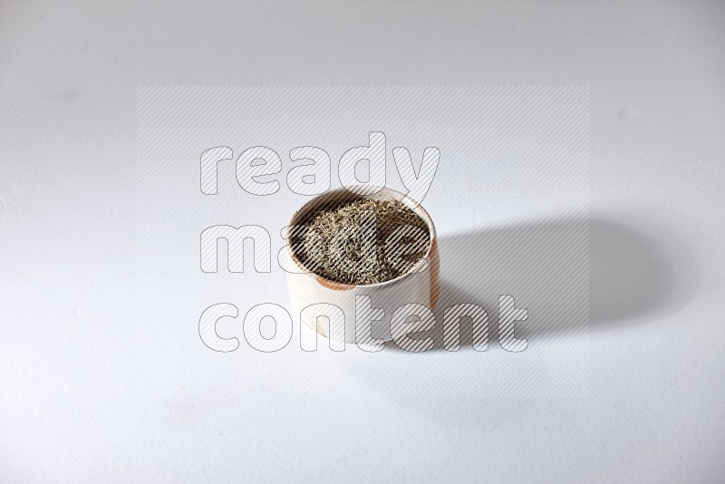 A beige bowl full of cumin seeds on a white flooring