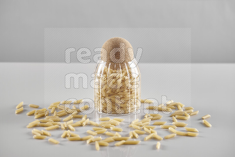 Raw pasta in a glass jar on light grey background