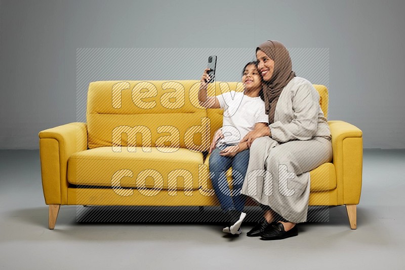 A girl sitting taking selfie with her mother on gray background
