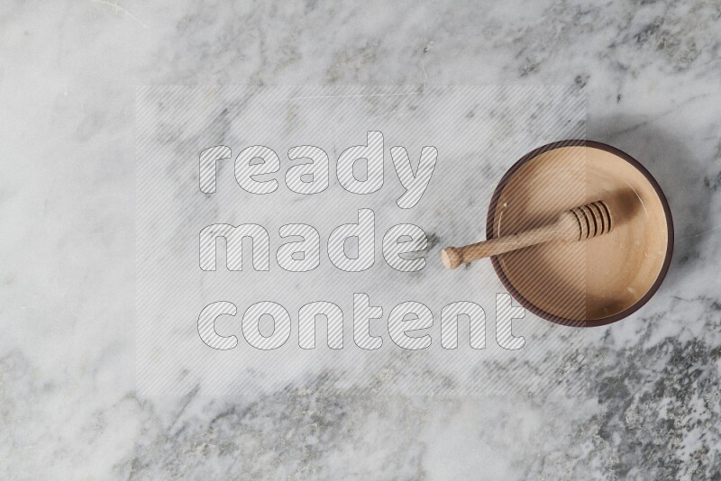 طبق فرن فخاري بيج مع ملعقة عسل خشبية بداخله على خلفية من الرخام الرمادي