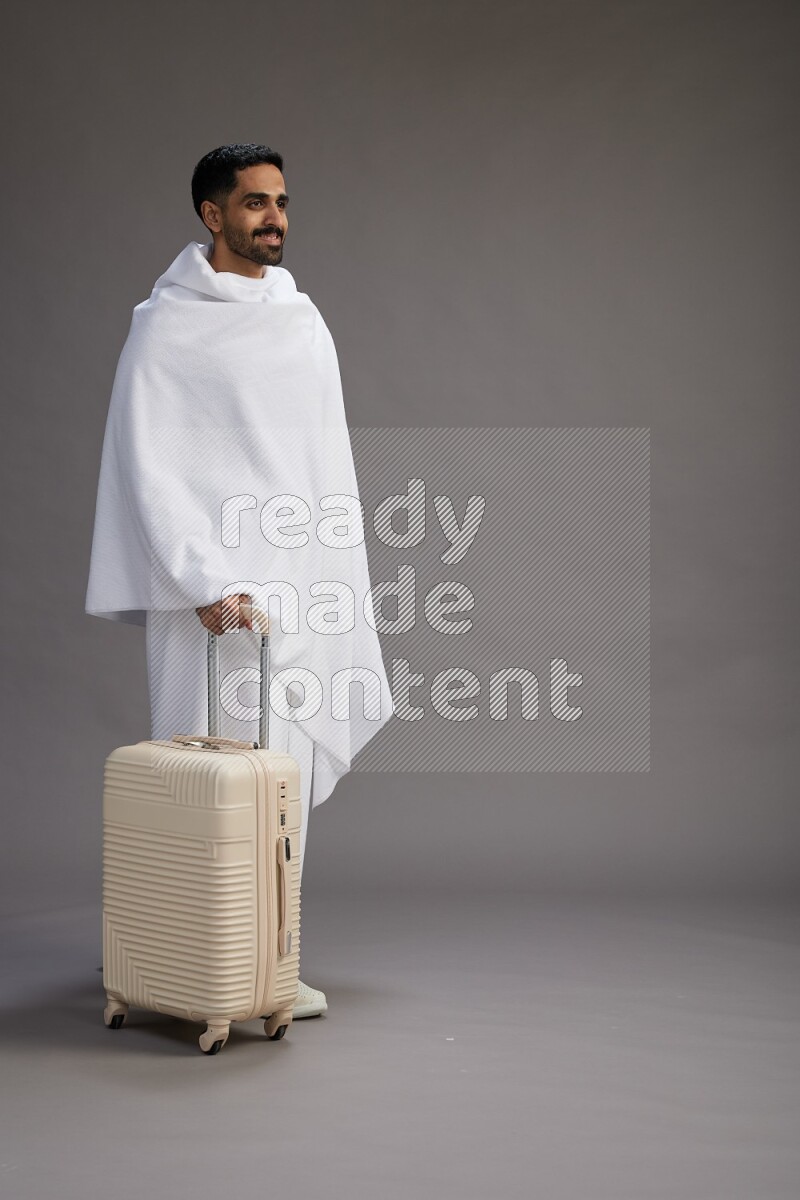 A man wearing Ehram Standing holding traveling bag on gray background