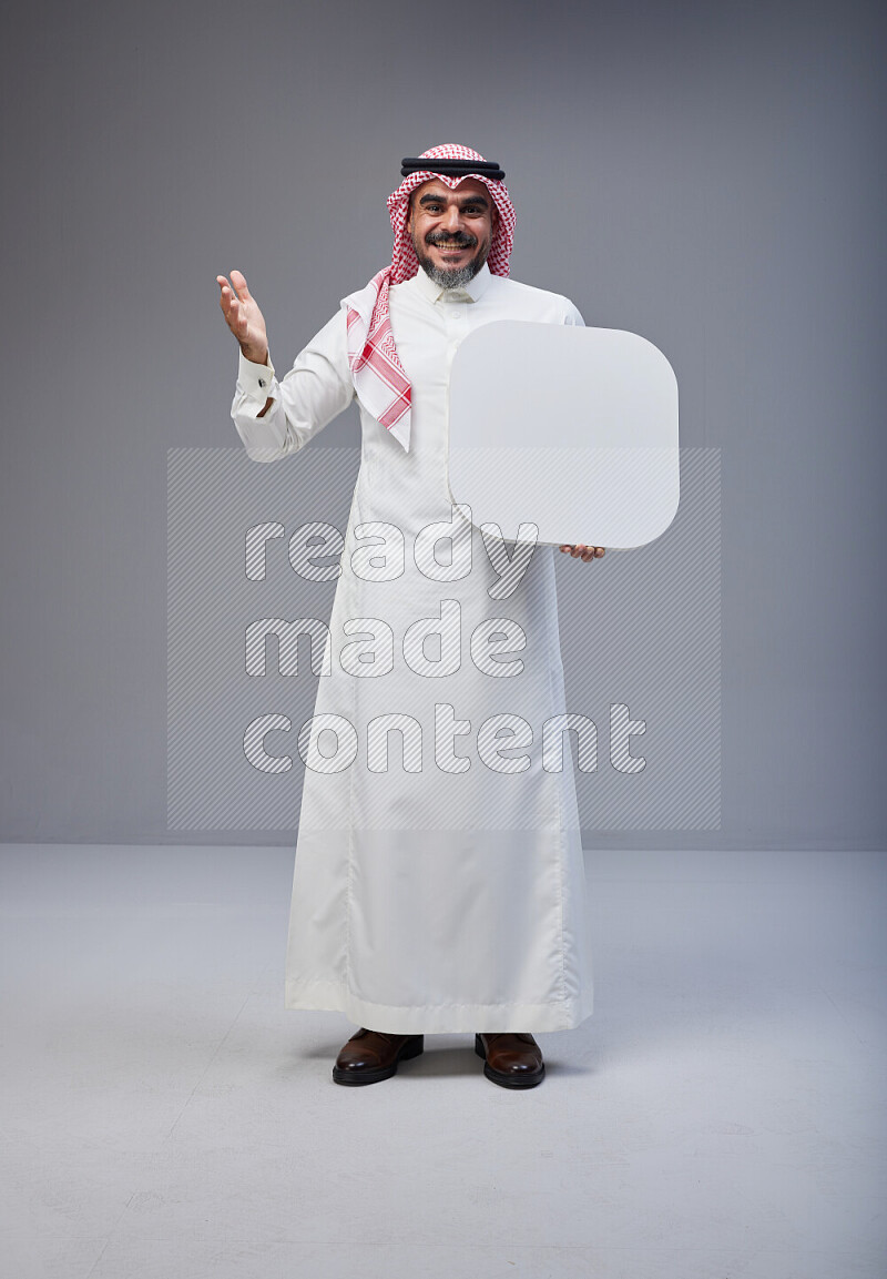 Saudi man Wearing Thob and red Shomag standing holding social media sign on Gray background