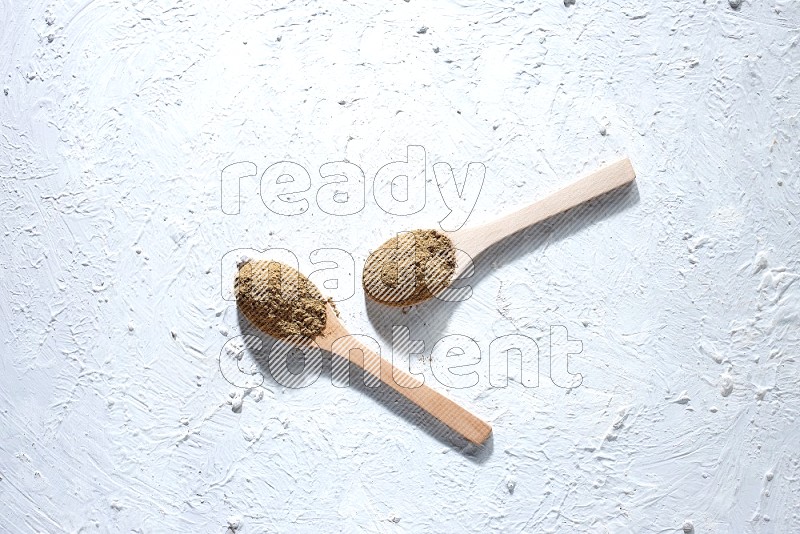 Wooden spoons full of allspice powder and allspice whole balls spreaded on a textured white flooring