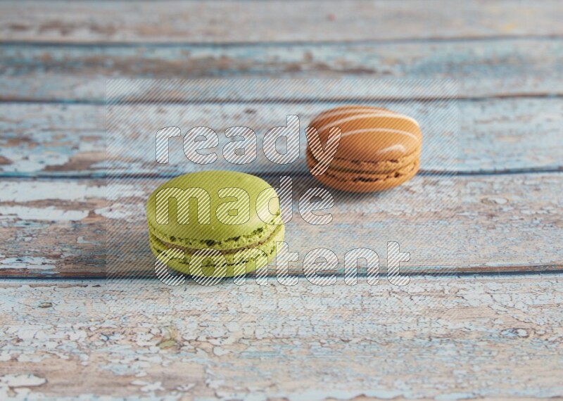 45º Shot of of two assorted Brown Irish Cream, and Green Pistachio macarons  on light blue background