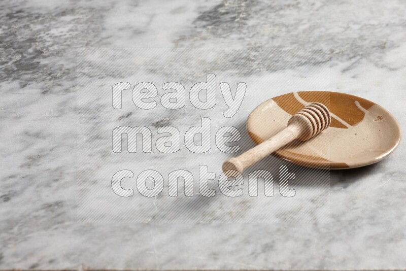 Multicolored pottery plate with wooden honey dipper in it on grey marble background
