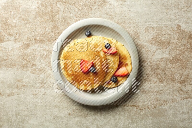 Three stacked mixed berries pancakes in a grey plate on beige background