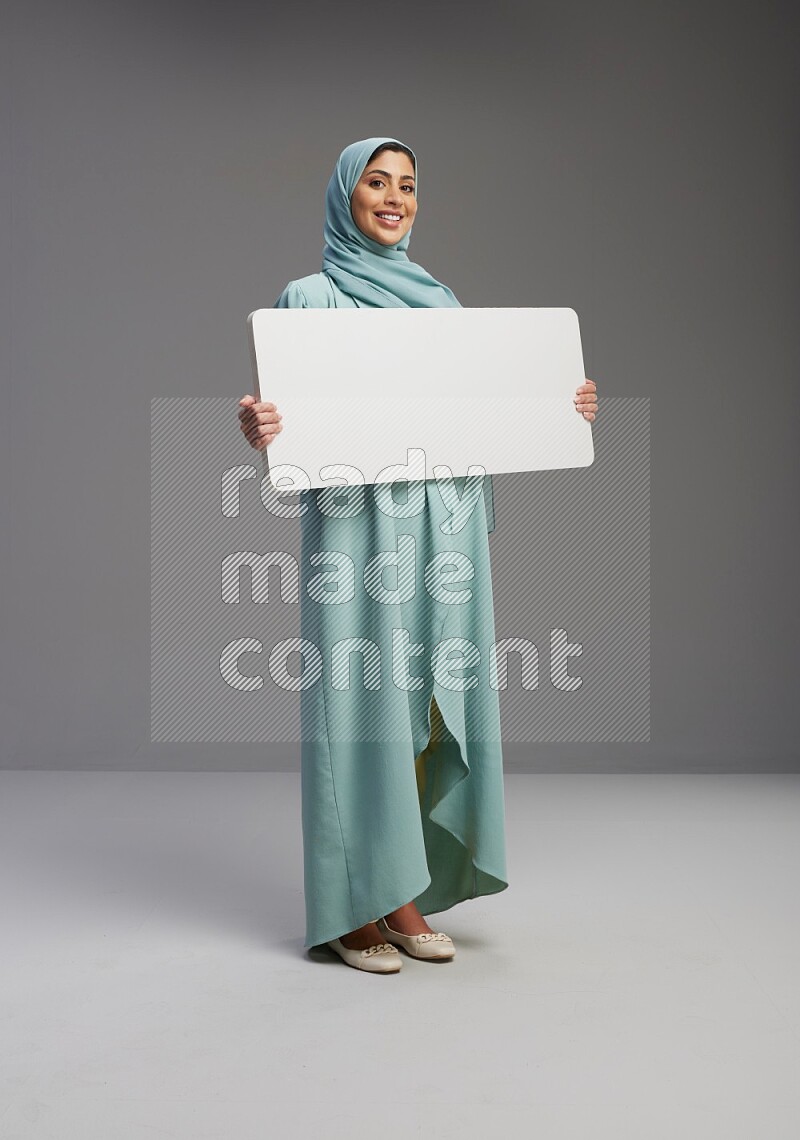 Saudi Woman wearing Abaya standing holding board on Gray background