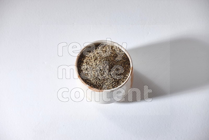 A beige bowl full of cumin seeds on a white flooring