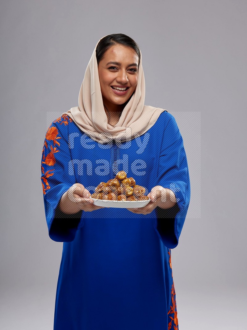 A Saudi woman standing wearing Jalabeya holding a plate of dates