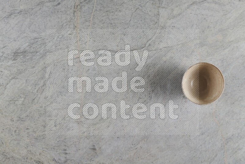 A small beige pottery bowl on grey marble background