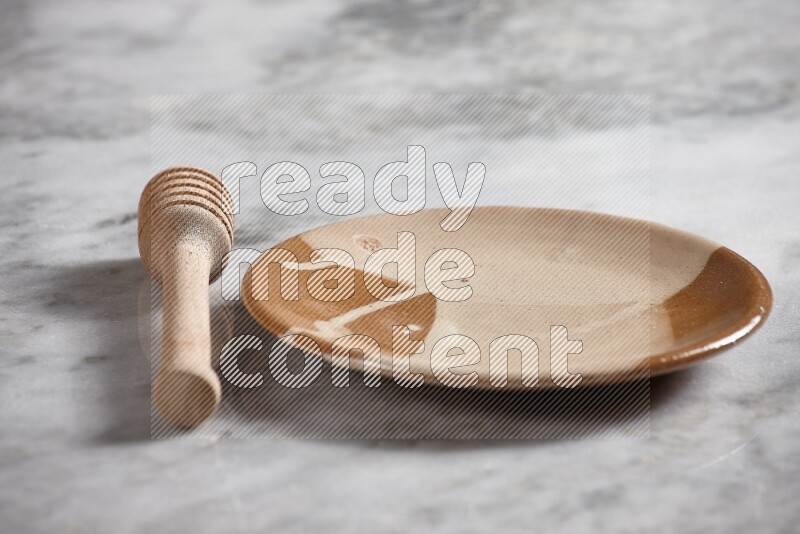 Multicolored pottery plate with wooden honey dipper on the side on grey marble background