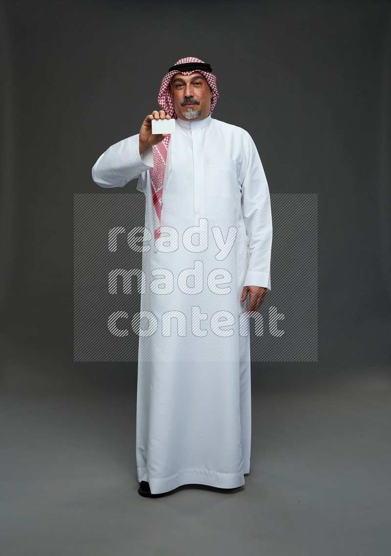 Saudi man with shomag Standing holding ATM card on gray background