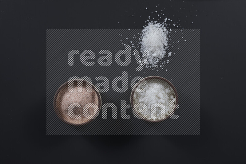 2 وعاء فخاري احدهمها ممتلئ بملح الهيمالايا والأخر بالملح الأبيض على خلفية سوداء