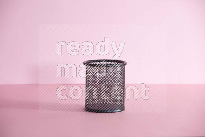 Pens, pencils and other different school supplies in a metal pen holder on rose background