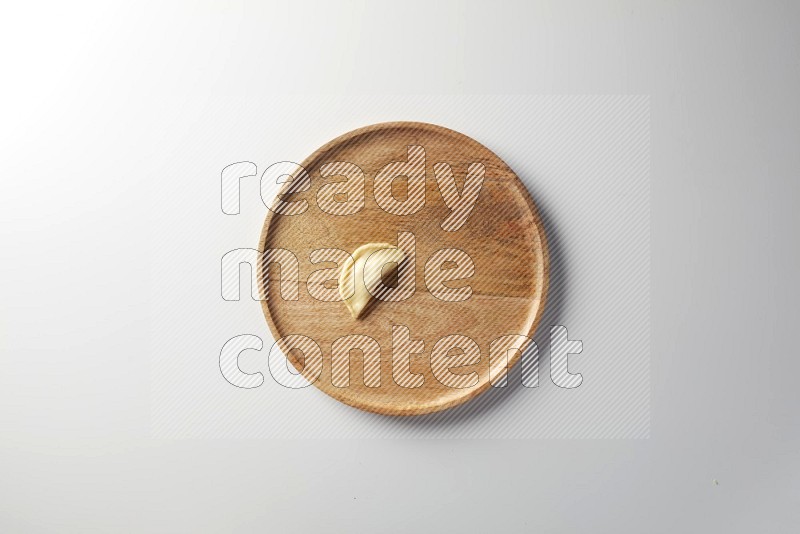 A single Sambosa on a wooden round plate on a white background